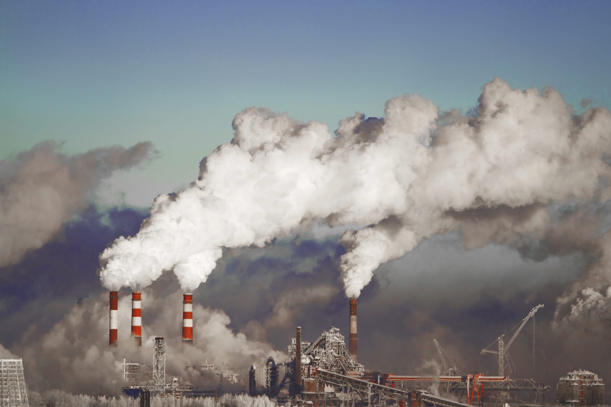 Industrial facility with multiple smokestacks emits large clouds of smoke into the sky, indicating air pollution.