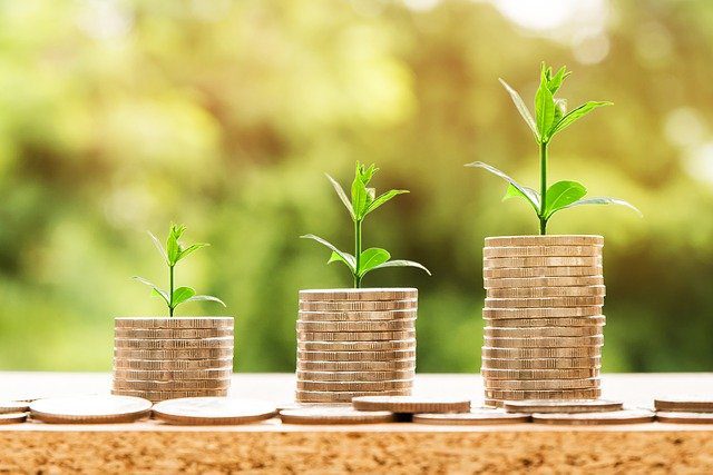 Three stacks of coins, each topped with a small green plant, shown in increasing height from left to right, symbolizing financial growth or investment.